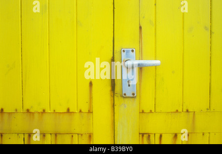 Detail der gelb gefärbten Holztür auf Schuppen, Hütte oder Messestand mit Aluminium Türgriff mit Rostflecken oder Kiosk hautnah Stockfoto