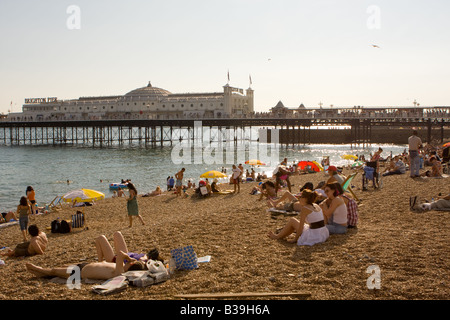 Leute, Sonnenbaden am Strand mit Brighton Pier im Hintergrund Stockfoto