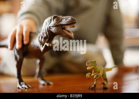 Modell Tyrannosaurus Rex in Händen der sechs Jahre alten Jungen Essen ein anderes Spielzeug Dinosaurier ein Velociraptor Stockfoto