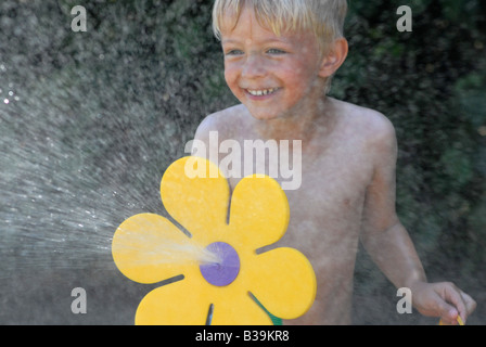 Kind spielt mit Gartenschlauch im Garten Stockfoto