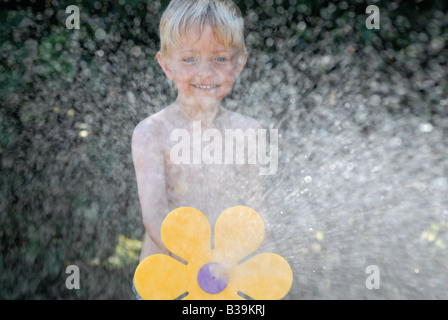 Kind spielt mit Gartenschlauch im Garten Stockfoto