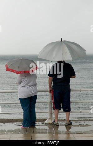 2 Personen im Sommer Urlaub Urlaub stehen im Regen unter Sonnenschirmen an Aberystwyth Strandpromenade August 2008 Stockfoto