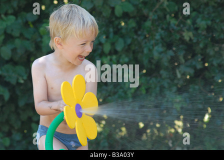 Kind spielt mit Gartenschlauch im Garten Stockfoto