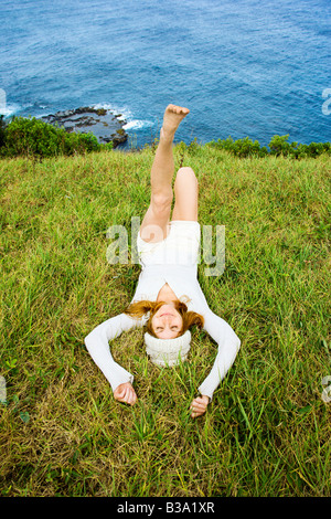 Fröhliche junge Frau entspannende Gras in der Nähe von Meer in Maui Hawaii Stockfoto