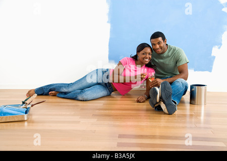 Afrikanische amerikanische paar entspannende zusammen mit Wein neben halb gestrichenen Wand und Malerei Zubehör Stockfoto