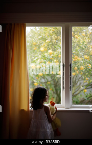 Mädchen im Alter von 5 blickt Fenster halten Stofftier Ente Stockfoto