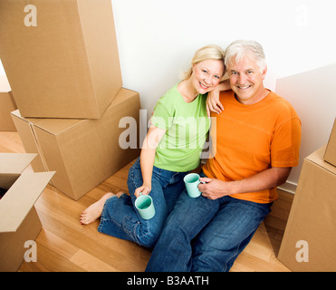 Mittleren Alter paar sitzt am Boden unter Karton Umzugskartons mit Kaffee Stockfoto