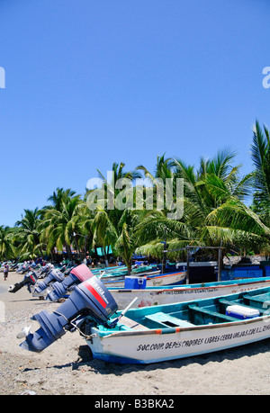 Fischerboote Playa Principal Zihuatanejo Mexiko | ZIHUATANEJO, Mexiko — Eine Reihe von Pangas am Strand, deren Yamaha-Außenbordwände erhöht sind, erstreckt sich entlang der Playa Principal unter einer Linie von Kokospalmen. Die Boote gehören lokalen Fischereigenossenschaften, die jeden Morgen den Fang der Bahía de Zihuatanejo anlanden, hauptsächlich Huachinango und andere Schnapper-Arten, die direkt auf dem Sand verkauft werden. Stockfoto