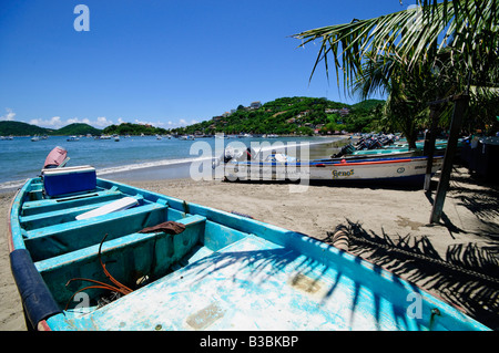 Panga-Fischerboot Playa Principal Zihuatanejo Bay | ZIHUATANEJO, Mexiko — Ein verwitterter Panga mit der Aufschrift „Soc. Ko. De Pescadores Libres Cerro Viejo' ruht am Playa Principal, da sich dahinter die Bucht von Zihuatanejo öffnet, die Boote und die Siedlung am Hügel über dem Wasser sichtbar sind. Der Name der Genossenschaft, der auf dem Rumpf eingemalt ist, bezeichnet eine rechtlich organisierte Fischereigesellschaft nach mexikanischem Recht, die den Mitgliedern kollektive Rechte an bestimmten Fischgründen und einem gemeinsamen Verkaufsunternehmen einräumt. Stockfoto
