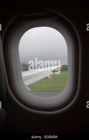 Suchen Sie ein Flugzeug Fenster am Flügel einer Boeing 737-800 bei Regen auf dem Fenster während der Landung Stockfoto