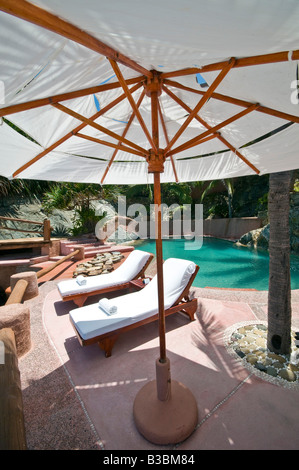 La Casa Que Canta Resort am Pool Zihuatanejo Mexiko | ZIHUATANEJO, Mexiko - zwei Liegestühle mit gerollten weißen Handtüchern sitzen unter einem Sonnenschirm neben dem türkisfarbenen Pool im La Casa Que Canta, einem Boutique-Resort, das in die felsige Küste der Zihuatanejo Bay an der mexikanischen Pazifikküste gebaut wurde. Steinmauern und einheimische Palmen umschließen die Terrasse, Teil eines Anwesens an den Klippen im mexikanischen Bundesstaat Guerrero. Stockfoto