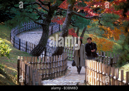 Zwei Frauen gehen einen gewundenen kopfsteingepflasterten Weg unter Herbst Bäume im berühmten Ritsurin-Garden in Takamatsu, Shikoku Stockfoto