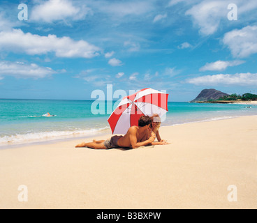 Junges Paar unter Sonnenschirm am Strand liegen Stockfoto