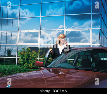 Geschäftsfrau sprechen über Handy stehen mit Auto vor Bürogebäude Stockfoto