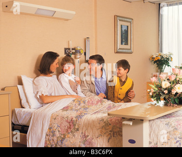 Krankenhaus. Vater und Kinder besuchen Mutter im Bett. Stockfoto