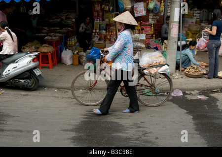 Eine Frau drückt ihr Fahrrad beladen mit Baguette in einer Straße Hanoi-Vietnam Stockfoto