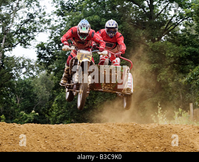 Motocross Seitenwagen Rennfahrer in Luft über Hügel mit Bäumen und Staub und sandige Strecke rot Stockfoto