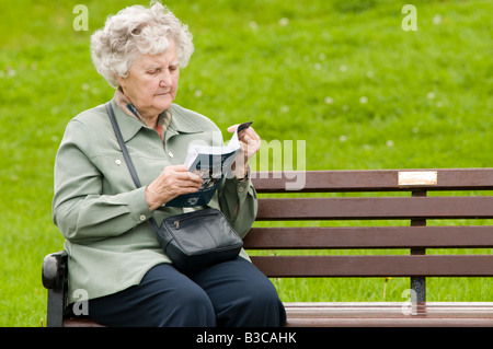 Ältere Frau im Urlaub sitzt alleine auf Parkbank, Tourist-Information lesen Prospekt Aberaeron Wales UK Stockfoto