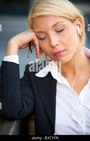 Junge Geschäftsfrau tragen Kopfhörer mit Augen geschlossen hält Brillen Stockfoto