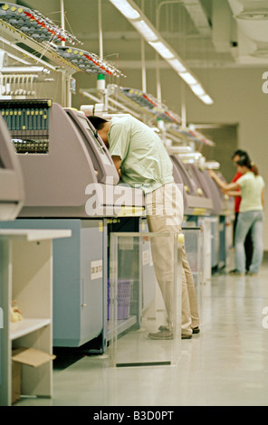 Ein Arbeiter schaut in eine Strickmaschine in einer Strickerei in Shanghai, China. Stockfoto