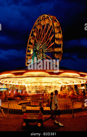 Vater zieht kleine Mädchen im Wagen neben Karussell mit Bewegung verwischen in der Abenddämmerung in der Kentucky State Fair Midway Stockfoto