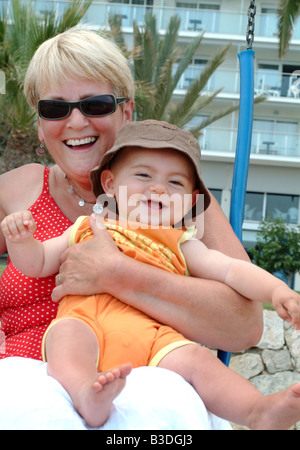 eine Großmutter und Enkel ihr Baby spielen zusammen auf einer Schaukel in einem park Stockfoto
