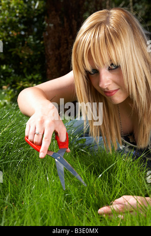 junge blonde behaarte Frau späten Teenager Anfang zwanzig schneiden Rasen in einem Garten mit einer Schere Stockfoto