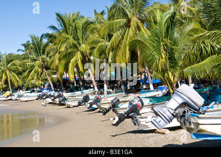 Fischerboote Playa Principal Zihuatanejo | ZIHUATANEJO, Mexiko – Pangas mit Außenbordantrieb, die zur lokalen Fischereigenossenschaft gehören, sitzen auf Playa Principal unter einem dichten Wald von Kokospalmen. Zihuatanejo ist einer der wenigen Ferienorte an der Pazifikküste Mexikos, wo sich noch immer eine handwerkliche Flotte den Hauptstrand der Stadt mit Besuchern teilt, ein Vermächtnis der 1970er Jahre, die große Hotelentwicklung stattdessen im benachbarten Ixtapa zu konzentrieren. Stockfoto