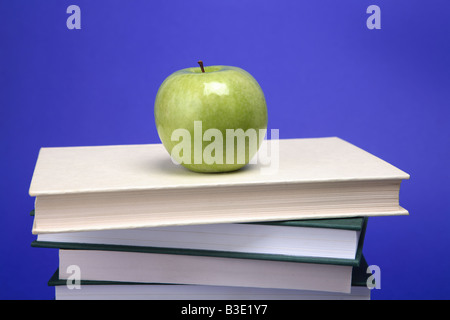 Ein grüner Apfel auf einem Stapel Bücher mit blauem Hintergrund Stockfoto