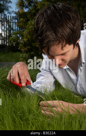 junge dunkelhaarig Mann späten Teenager Anfang zwanzig schneiden mit der Schere in einem Garten Rasen Stockfoto