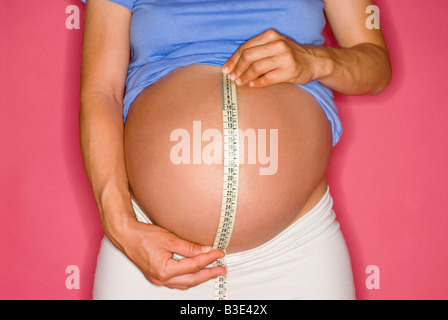 SCHWANGERE FRAU IHREN BAUCH MIT EINEM MAßBAND MESSEN. SCHWANGERSCHAFT Stockfoto