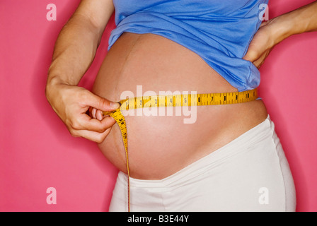 SCHWANGERE FRAU IHREN BAUCH MIT EINEM MAßBAND MESSEN. SCHWANGERSCHAFT Stockfoto