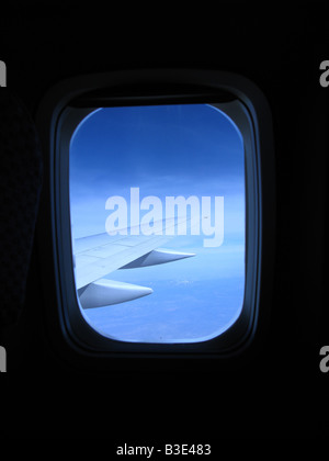 Suchen Sie ein Flugzeug Kabinenfenster mit Blick auf den Flügel und blauer Himmel Stockfoto