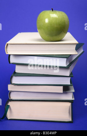 Ein grüner Apfel auf einem Stapel Bücher mit blauem Hintergrund Stockfoto