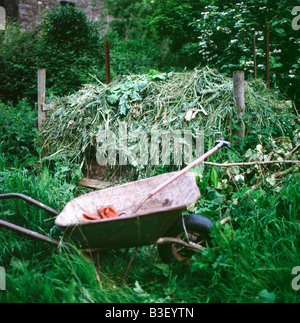 Komposthaufen, Ungräser in eine Schubkarre, Gabel und Gartenhandschuhe in einer autarken Garten in Wales UK KATHY DEWITT Stockfoto