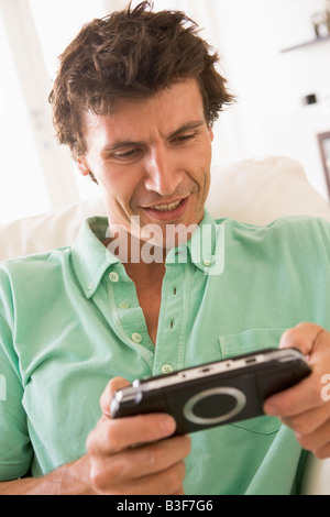 Mann im Wohnzimmer spielen handheld Videospiel lächelnd Stockfoto