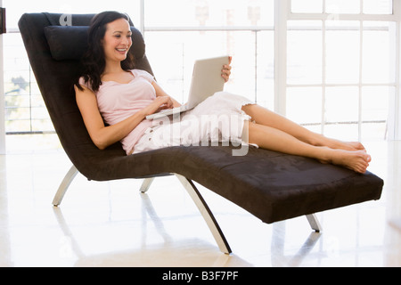 Frau sitzt im Stuhl mit Laptop lächelnd Stockfoto