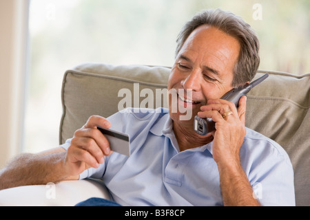 Mann im Haus mit Telefon und Kreditkarte lächelnd zu betrachten Stockfoto