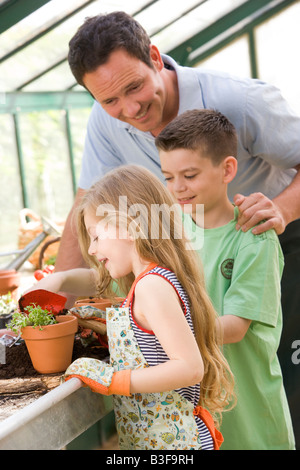 Mann im Gewächshaus helfen zwei kleine Kinder, die Erde im Topf setzen Stockfoto