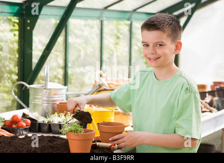 Kleiner Junge im Treibhaus Erde im Topf lächelnd setzen Stockfoto