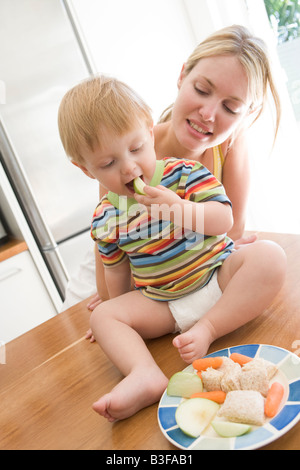 Mutter und Baby in Küche essen Obst und Gemüse Stockfoto