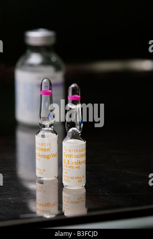 Zwei Ampullen Syntocinon (Oxytocin) Medikament auf Stahltisch mit einer Flasche eines Lokalanästhetikums im Hintergrund Stockfoto