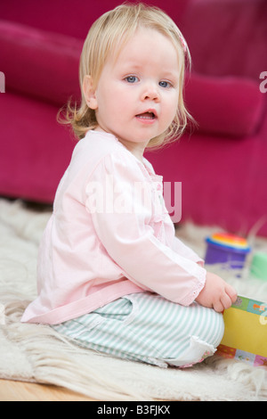 Baby im Wohnzimmer mit Spielzeug und Buch Stockfoto