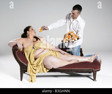 Große dicke übergewichtige Frau Kuchen gefüttert werden, während auf einer Chaiselongue liegen. Stockfoto
