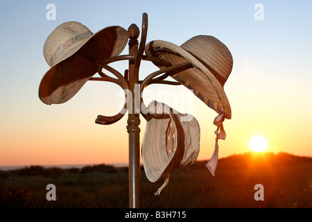 drei Stroh Urlaub Sonnenhüte auf einem hölzernen Hatstand gegen eine untergehende Sonne Stockfoto