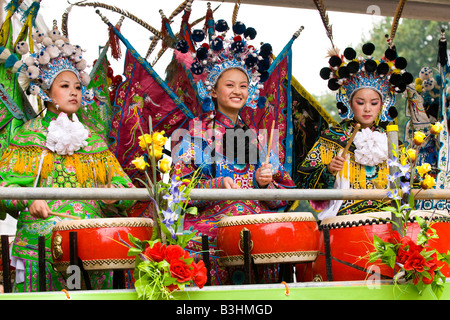 Notting Hill Carnival Parade, schöne junge chinesische Mädchen im Teenageralter Schlagzeug in exotischen Trachten lachen Stockfoto