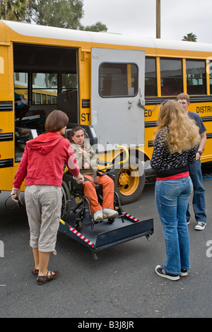 Einen Rollstuhl special Needs, die Schüler in der Schule über behindertengerechte Aufzüge auf einen modifizierten Schulbus Lehrer ankommt trägt Handschuhe Stockfoto