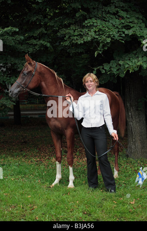 Die Blondine posiert mit einem Araberhengst am park Stockfoto