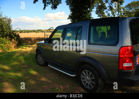A Land Rover Discovery 3 parked in the shade of a tree at the entrance to a field of wheat Stockfoto