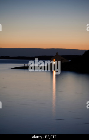 Einem hellen Fensterlicht strahlt über die noch Loch Bucht von einem abgelegenen Haus in Stein, Waternish Punkt auf der Isle Of Skye. Stockfoto